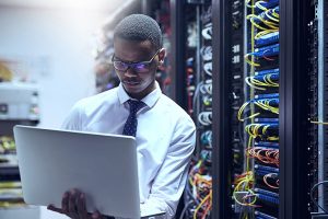 Cropped shot of a IT technician working on his laptop while standing inside of a server room